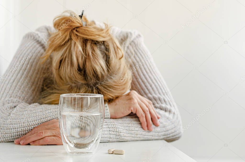 Elderly woman feeling stressed. Selective focus on glass and pills. Depression treatment concept