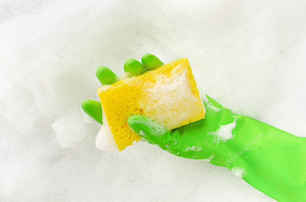 Hand in protective glove holding a soapy sponge on foam background. Dish washing concept. Copy space