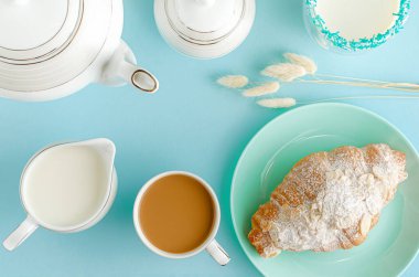 Kahvaltı arkaplanı. Turkuaz tabakta taze kruvasan, bastel mavi masada süt ve kahve. Üst manzara, düz uzanma