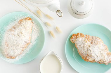 Kahvaltı arkaplanı. Turkuaz tabakta taze kruvasan ve beyaz masada süt kavanozu. Üst manzara, düz uzanma