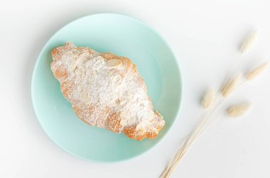 Turkuaz tabakta kahvaltıda taze pişmiş kruvasan. Tepede, en üstte. Beyaz arkaplan