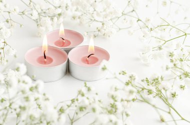 Beyaz arka planda çiçeklerle süslenmiş yanan aroma mumları. SPA ve güzellik konsepti.