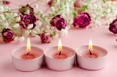 Aromaterapi konsepti. Üç yanan mum ve pembe arka planda kuru güller..
