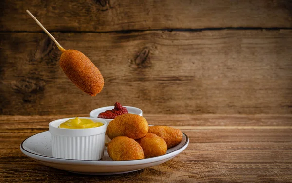 American street food concept. Corn dogs with mustard on wooden background with copy space