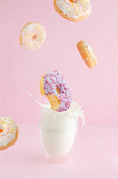 Bitten donut with fruit flavor falling into the glass of milk with splash. Flying food concept. Vertical