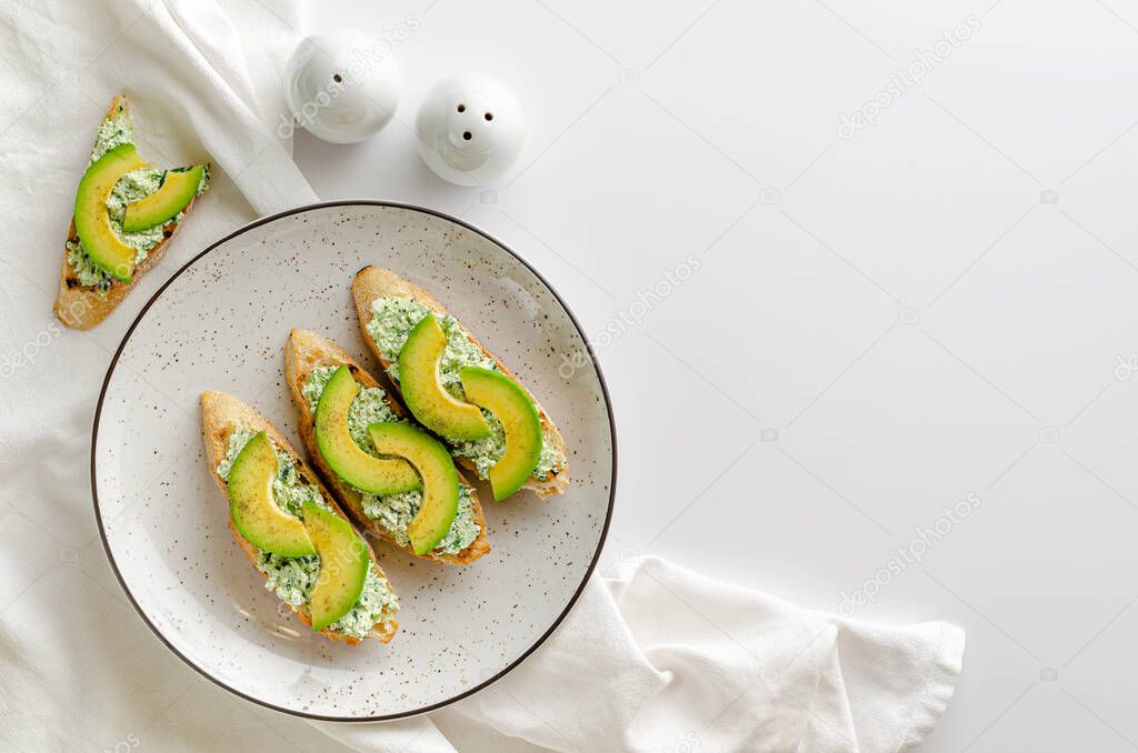 Healthy eating concept. Toasted baguette slices with ricotta, spinach and avocado on white table. Copy space