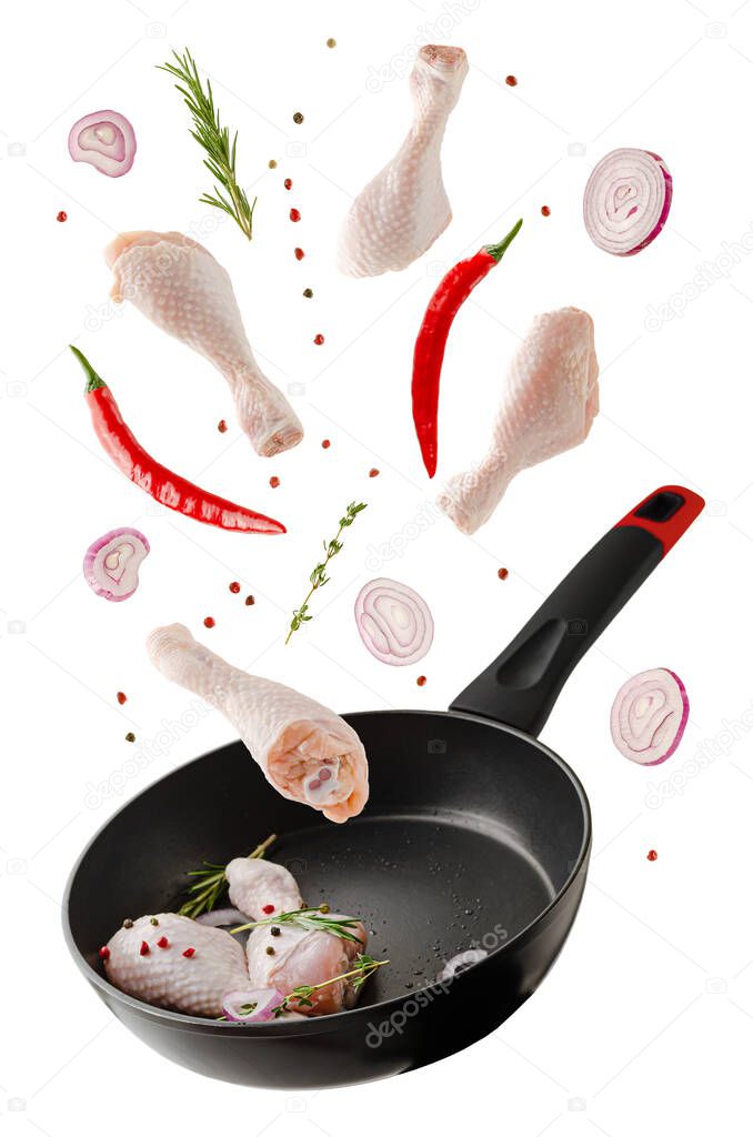 Flying raw chicken legs or drumsticks with spices over frying pan isolated on white. Food levitation concept