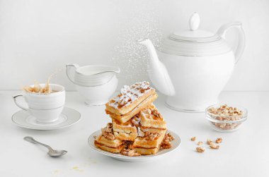 Viyana gofretlerine cevizli şeker tozu dökülüyor ve kahvaltı masasına kahve sıçrıyor. Beyaz arkaplan