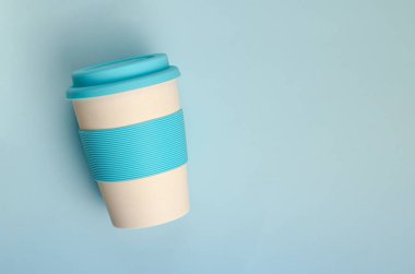 Pastel mavi arka planda silikon tutacağı olan yeniden kullanılabilir plastik ücretsiz bambu bardağı. Üst görünüm, boşluğu kopyala. Sıfır atık.