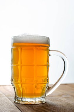 Beyaz ahşap arka planda bir bardak dolusu sarı bira. Dikey, boşluğu kopyala