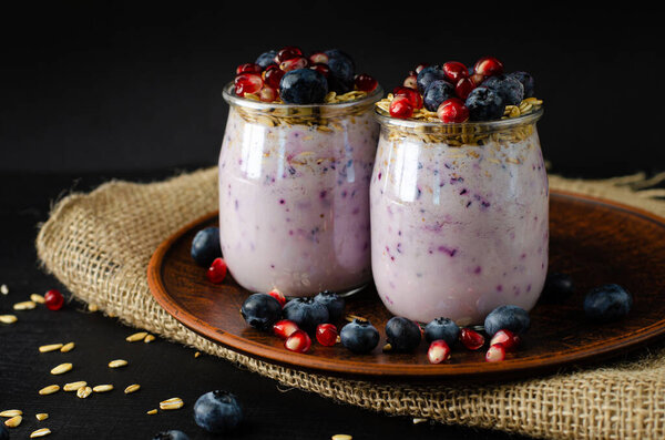 Close up shot of yogurt with blueberries, pomegranate seeds and oats on dark background. Front view
