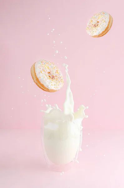 Splashing glass of milk and flying donuts with sprinkles on pink background. Copy space. Levitation food concept.