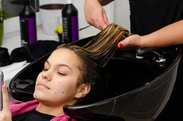 Hair stylist applying hair mask and combing clients wet hair with brush in a black sink.