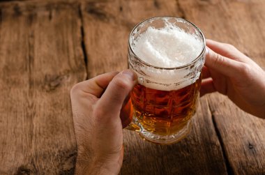Koyu ahşap arka planda bira bardağı tutan bir adamın elleri. Alkolik içki konsepti