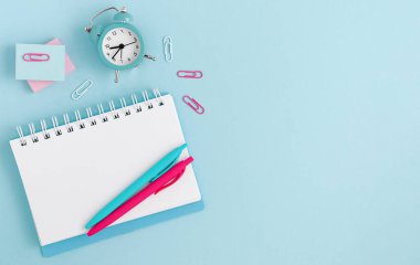 Şablon modeli. Pastel mavi arka planda defter, saat ve kalemlerle çalışma alanı. Üst Manzara. Boşluğu kopyala