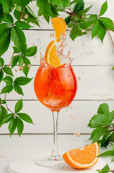 Portakal dilimleri aperol kokteyline dökülüyor. Beyaz ahşap arka planda serinletici İtalyan yaz içeceği.