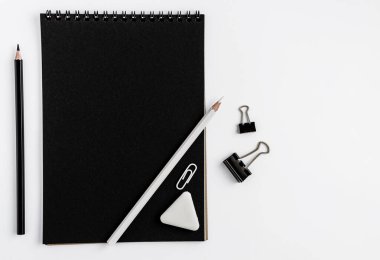 Siyah defter boş maketi, beyaz arka planda kalemler ve kırtasiye malzemeleri. Üst görünüm, alanı kopyala