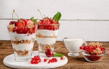 Tahta zemin üzerinde taze frenk üzümü, kiraz, çilek ve yoğurt bulunan granola.