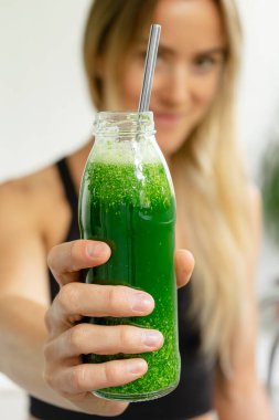 Elinde bir şişe yeşil detoks brokoli, ıspanak ve salatalık tutan genç bir kadın..