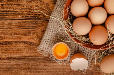 Kahverengi yumurtalar kasede ve kırık yumurta ile ahşap arka planda yumurta sarısı. Tam üstte