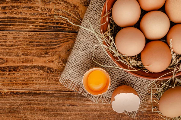 Kahverengi yumurtalar kasede ve kırık yumurta ile ahşap arka planda yumurta sarısı. Tam üstte