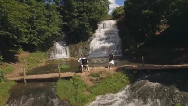 Вид с воздуха. Два музыканта пианист и бандура играют на скалах у водопада — стоковое видео