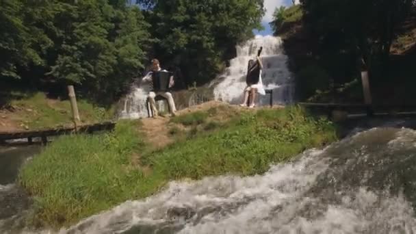 Vista aérea. Dos músicos Pianista y bandura tocando en las rocas en la cascada — Vídeos de Stock