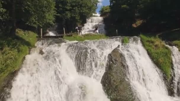 Вид с воздуха. Два музыканта пианист и бандура играют на скалах у водопада — стоковое видео