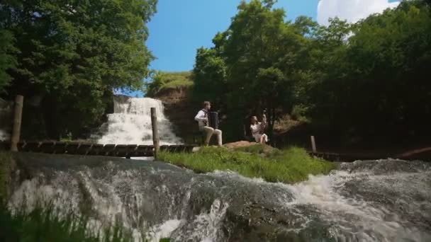Two musicians Pianist and bandurist playing on the rocks at waterfall — Stock Video