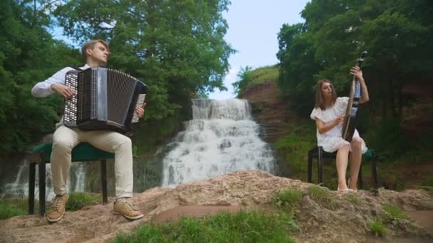 Twee muzikanten Pianist en bandurist spelen op de rotsen bij de waterval — Stockvideo