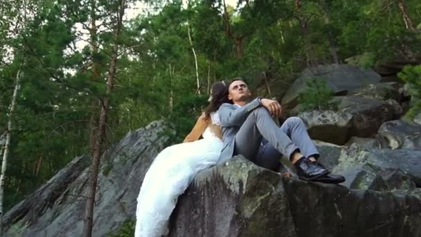 Casal sentado em rochas com floresta no fundo. Movimento lento — Vídeo de Stock