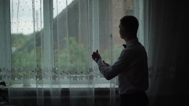 El joven admira la vista desde la ventana de su casa y se pone una camisa. Movimiento lento — Vídeos de Stock