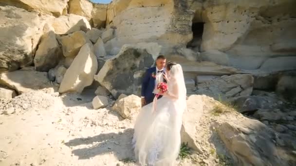 Bruid en knappe bruidegom lopen in de buurt van zandstrand rotsen — Stockvideo