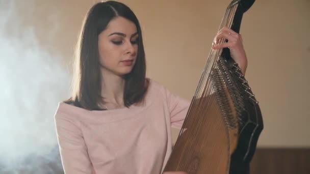 Jonge Oekraïense vrouw speelt een traditioneel bandura-instrument in de lichte kamer — Stockvideo