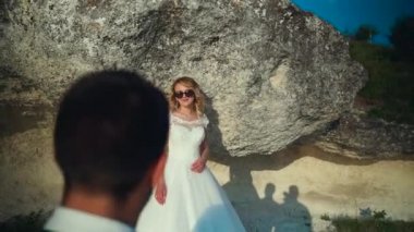 Çift okyanus kayalıklarına doğru yürür, birlikte manzaraya bakar. Yavaş çekim