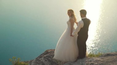 Çift okyanus kayalıklarına doğru yürür, birlikte manzaraya bakar. Yavaş çekim.