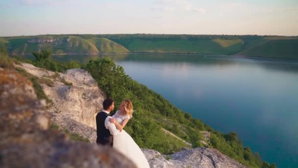 Pár óvatosan ölelés állva szélén a szikla, és keresi a tavon — Stock videók