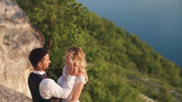 Пара нежно обнимаются стоя на краю скалы и глядя на озеро — стоковое видео