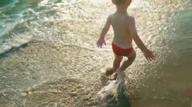 Mutlu çocuk koşmak ve neşeyle atlamak ve gün batımında deniz suyuna sıçrayan. Slowmo