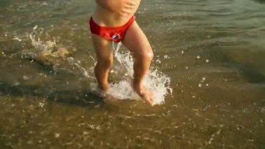 Mutlu çocuk koşmak ve neşeyle atlamak ve gün batımında deniz suyuna sıçrayan. Slowmo