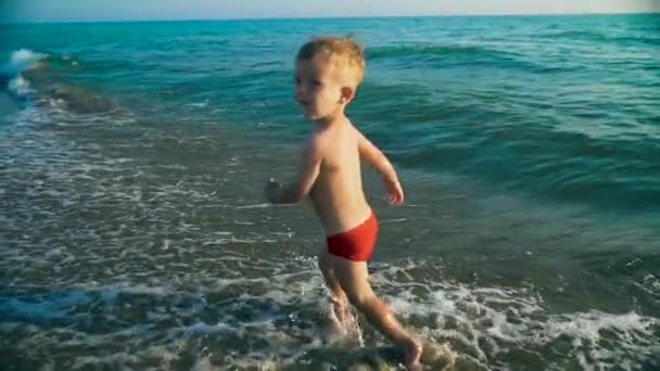 Happy boy run and jump merrily and splashing in the sea water in sunset. Slowmo — Stock Video