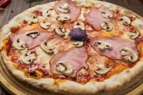 Delicious italian pizza with ham and mushrooms on wooden background