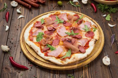 Lezzetli İtalyan pizza jambon, Bavyera sosis ve fesleğen tarafından dekore edilmiş prosciutto ile ahşap arka plan üzerinde bırakır