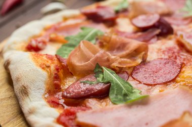 Lezzetli İtalyan pizza jambon, Bavyera sosis ve fesleğen tarafından dekore edilmiş prosciutto ile ahşap arka plan üzerinde bırakır