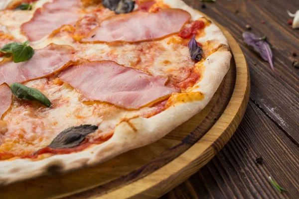 Delicious italian pizza with ham and basil leaves on wooden background