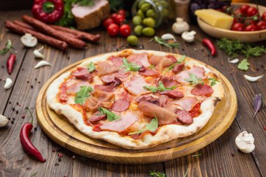 Lezzetli İtalyan pizza jambon, Bavyera sosis ve fesleğen tarafından dekore edilmiş prosciutto ile ahşap arka plan üzerinde bırakır