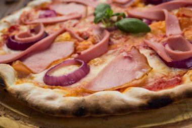 Lezzetli İtalyan pizza jambon, sosis ve fesleğen tarafından dekore edilmiş soğan ile ahşap arka plan üzerinde bırakır