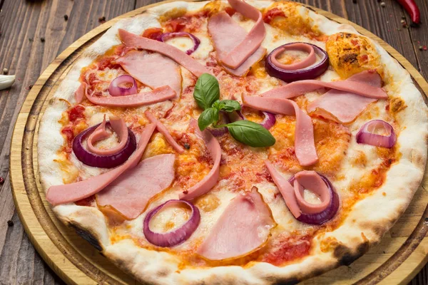 Lezzetli İtalyan pizza jambon, sosis ve fesleğen tarafından dekore edilmiş soğan ile ahşap arka plan üzerinde bırakır