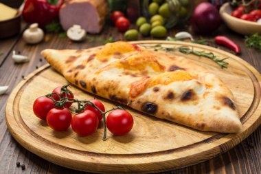 Geleneksel İtalyan kapalı pizza Calzone fesleğen ile ahşap arka plan üzerinde bırakır
