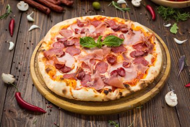 Lezzetli İtalyan pizza jambon, Bavyera sosis ve fesleğen tarafından dekore edilmiş prosciutto ile ahşap arka plan üzerinde bırakır
